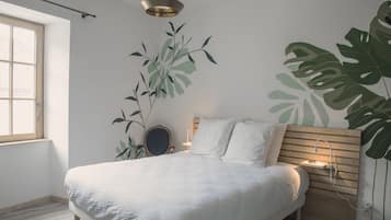 A bedroom with a bed, a bedside table, a lamp, a window, and wall art.