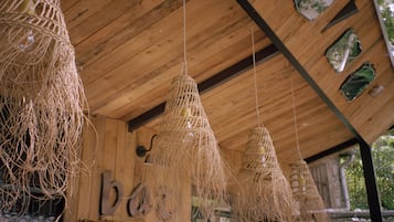 Un interior rústico de madera con lámparas colgantes tejidas y un letrero de 'b' visible, indicando una zona de bar.