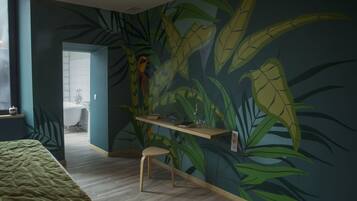 Una habitación con una cama, un taburete de madera, una estantería con objetos y un baño al fondo.
