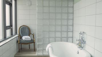 Ein Badezimmer mit einer freistehenden Badewanne, einem Holzstuhl und einer Duschkabine aus Frostglas.