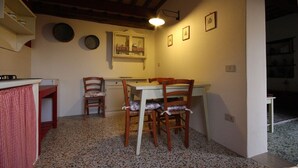 Uma cozinha compacta com uma mesa de jantar e cadeiras, uma pequena geladeira e uma prateleira na parede com louças.