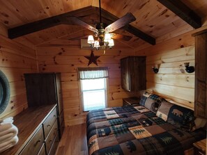 Een knus slaapkamer in een houten hut met een bed, een dressoir en een ster decoratie aan het plafond.