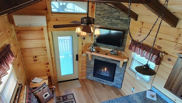 Ein gemütliches Cabin-Interieur mit Kamin aus Stein, Holzwänden, Deckenventilator und einem großen Fernseher.