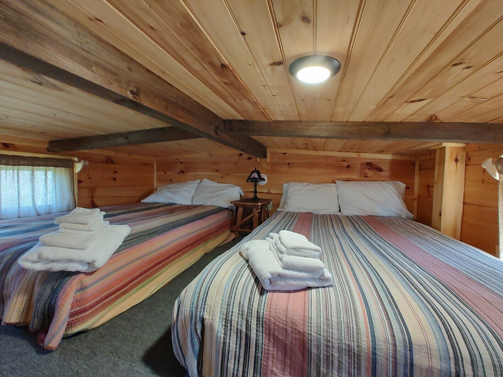 A cozy cabin room with two beds, each with striped bedding and neatly folded towels.