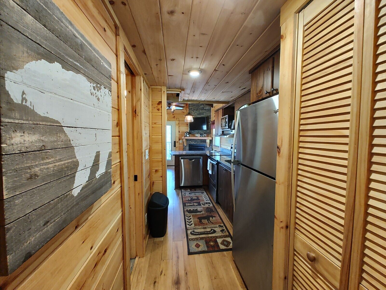 A narrow wooden hallway with a kitchen area on the right, featuring a refrigerator and a microwave.