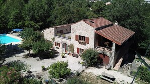 Une maison en pierre avec une piscine, entourée d’arbres et de collines.