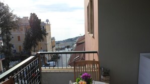 A balcony with a table and chair, overlooking a street with buildings and parked cars. - Home Away From Home (Monterosso al Mare)