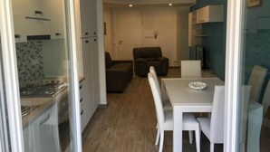 A modern kitchen with white cabinets and a built-in stove, a dining area with a white table and chairs, and a living room with a brown sofa and a TV. - Home Away From Home (Monterosso al Mare)
