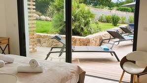 A bedroom with a bed, a chair, and a view of an outdoor area with a pool and lounge chairs. - Villa Maria 2. 12 pers, piscine chauffée, 5 min plage (sainte lucie de porto vecchio)