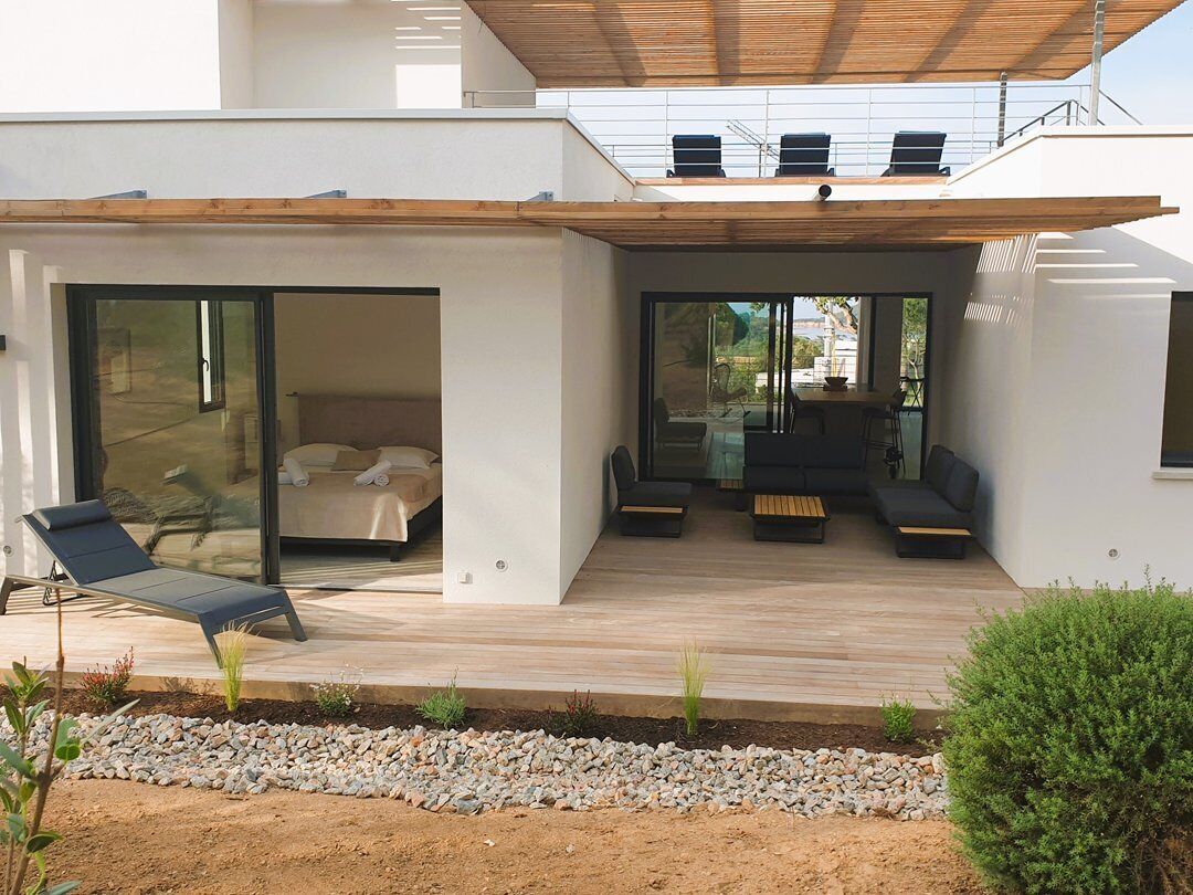 A modern house with a covered patio, a sliding glass door leading to a bedroom, and a seating area with a table and chairs.