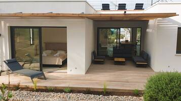 A modern house with a covered patio, a sliding glass door leading to a bedroom, and a seating area with a table and chairs.