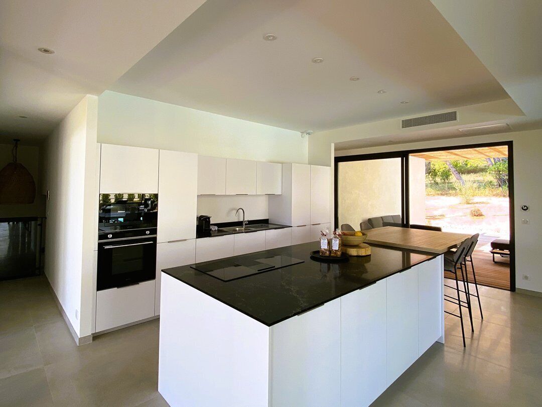 Een moderne keuken met witte kasten, een centraal eiland en een eethoek met uitzicht op de omgeving.