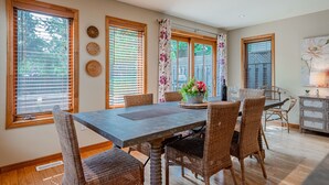 Un espace repas comprenant une table et des chaises, de grandes fenêtres équipées de stores et un mur décoratif.