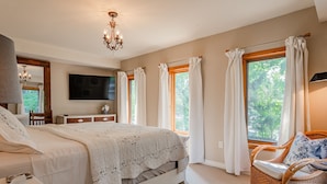 Une chambre à coucher avec un lit, une chaise, un téléviseur et des fenêtres avec des rideaux.
