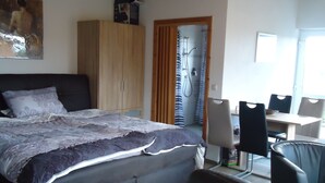 Une chambre comprenant un lit, une armoire en bois, un espace douche et une table à manger avec des chaises.