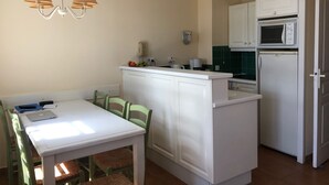 A compact kitchen with a white countertop, a built-in oven, and a microwave. There is a dining area with a white table and green chairs. - St Raphaël/App 4 pers/superb sea view/pool/wifi/climate (Saint-Raphaël)