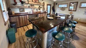 Una cocina con una isla central, taburetes de bar, detalles de madera y diverso menaje de cocina.