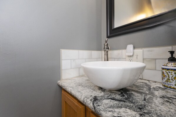 A bathroom with a white vessel sink, a marble countertop, and a soap dispenser.