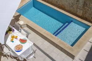 A rectangular pool with a tiled edge, a white table with a watermelon and drinks, and a chair. - Village house with pool, 3 bedrooms, 2 bathrooms, barbecue (Campanet)