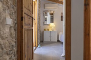 A hallway with a wooden door, a white cabinet with a mirror, and a bed with a white headboard.