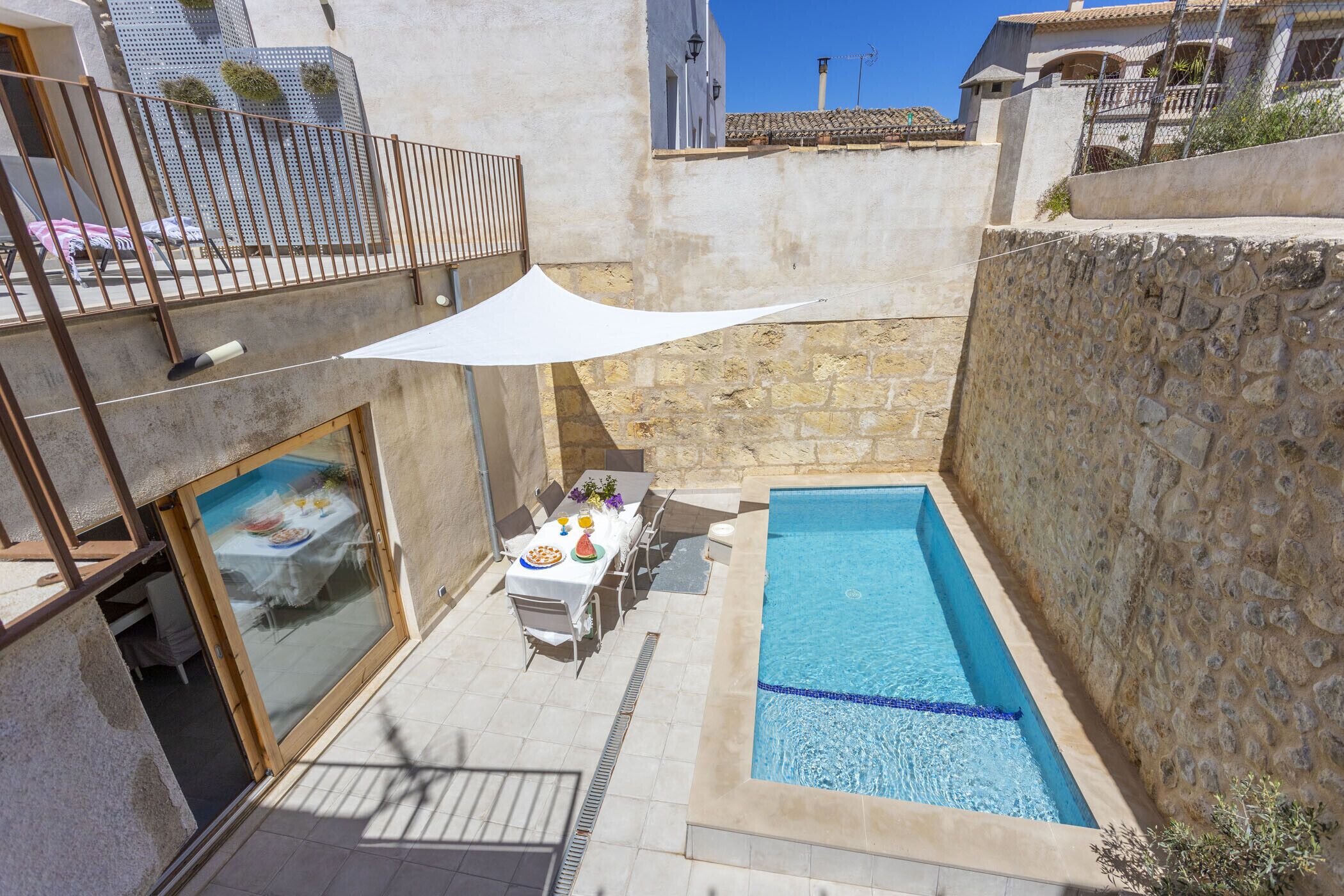 Un área de piscina con una mesa dispuesta para comer, un espacio de estar cubierto y un muro de piedra.