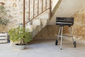 A stone staircase, a potted plant, and a barbecue grill in a tiled room.
