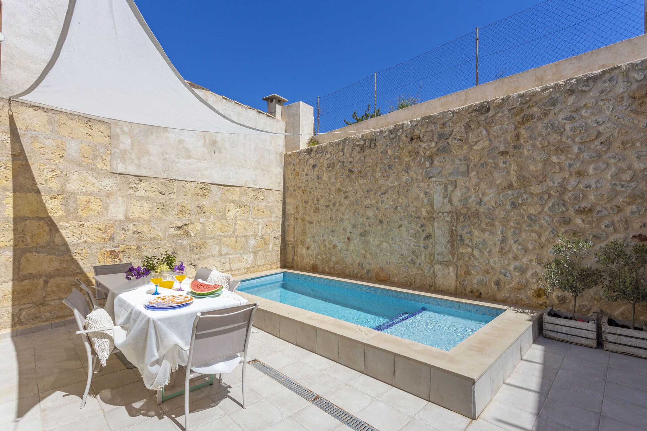 Une piscine bordée d’un mur en pierre, une table recouverte d’une nappe blanche et une chaise.