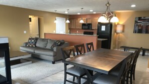A modern kitchen with a central island, a dining area with a wooden table and chairs, and a living room with a sofa and a coffee table. - Bay View, Downtown Traverse City Condo (Traverse City)