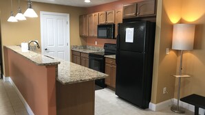 A kitchen with granite countertops, a black refrigerator, wooden cabinets, a microwave, and a floor lamp. - Bay View, Downtown Traverse City Condo (Traverse City)