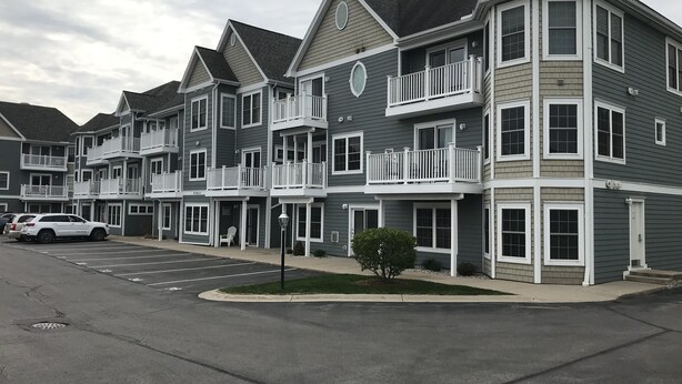 A multi-story residential building with balconies, a parking lot, and a small tree. - Bay View, Downtown Traverse City Condo (Traverse City)