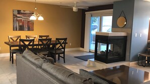 A living room with a sofa, dining table, chairs, a fireplace, and a ceiling fan. - Bay View, Downtown Traverse City Condo (Traverse City)
