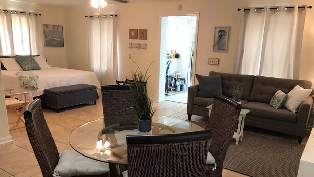 Une chambre d’hôtel comprenant un lit, un canapé, un coin repas avec des chaises en osier et une table en verre.