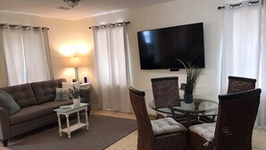 Un salon comprenant un canapé, une table avec un plateau en verre, des fauteuils en osier, un téléviseur à écran plat et une plante en pot.