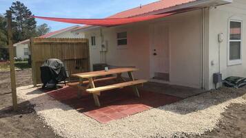 A covered outdoor area with a picnic table, a covered stroller, and a building with a red roof.