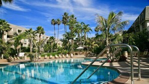 Una piscina con sillas de descanso y palmeras, rodeada de edificios de hotel.