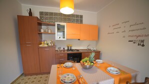 A compact kitchen with wooden cabinets, a dining table set with plates, cutlery, and a fruit bowl. - Lamezia Terme family apartment "girasoli" (Lamezia Terme)