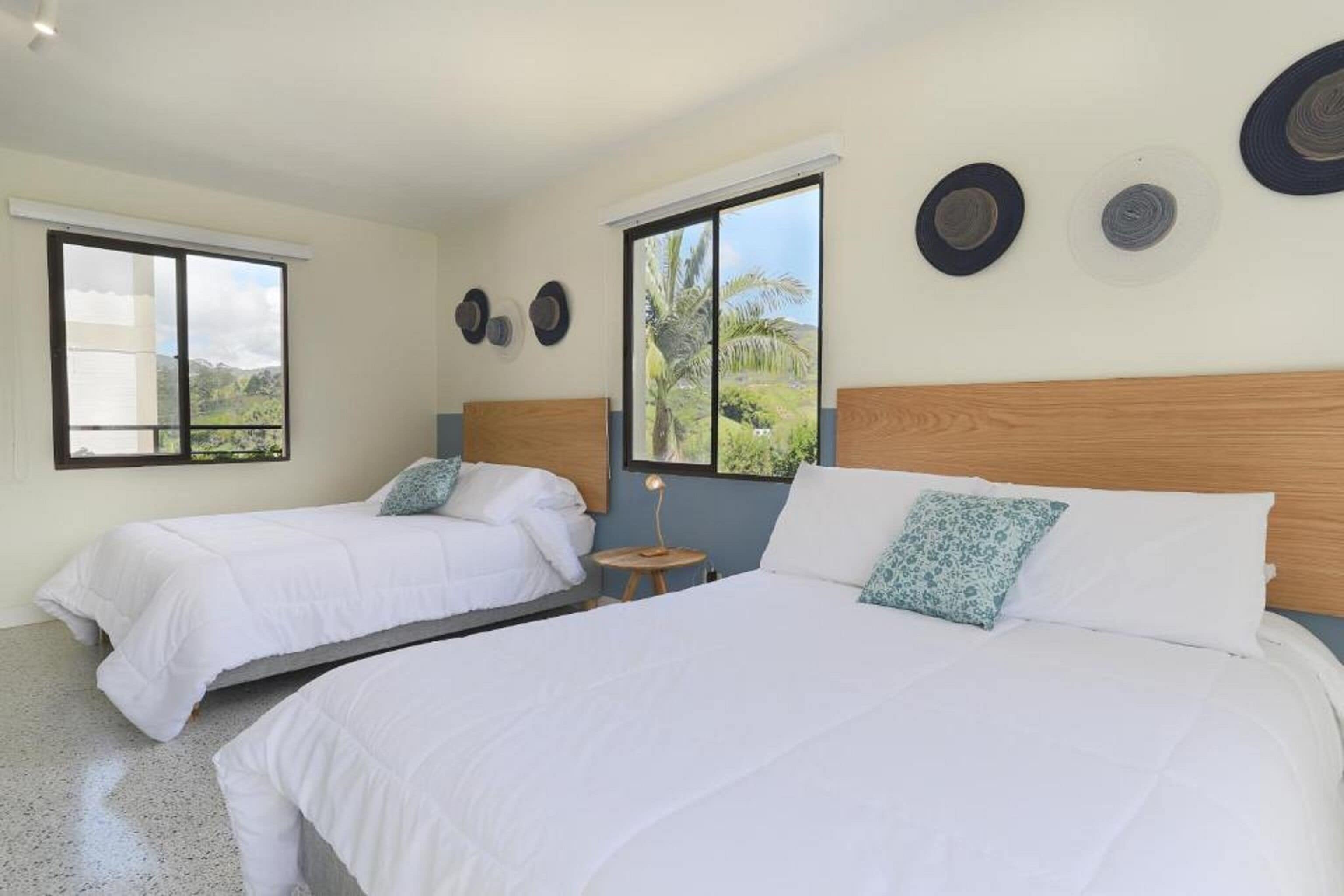 A hotel room with two beds, a small table, and a window with a view of greenery.