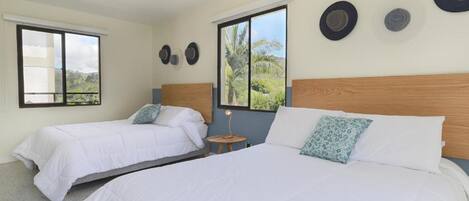 A hotel room with two beds, a small table, and a window with a view of greenery.