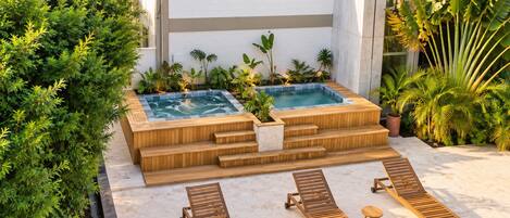 A spa area with two hot tubs, wooden steps, and lounge chairs.
