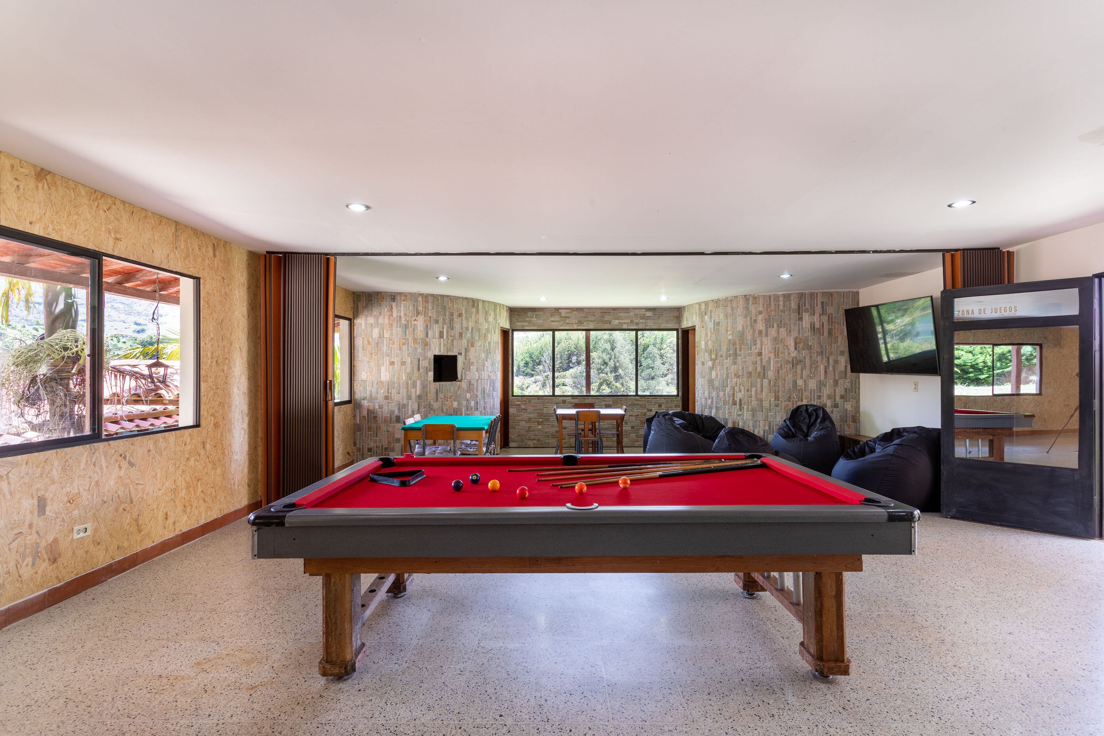 Uma mesa de bilhar em um espaço com vista para o exterior, uma televisão e uma área de estar com mesa e cadeiras.