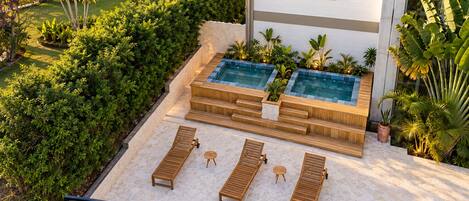 Un espace piscine aménagé sur le toit, avec des chaises longues en bois et une petite table, entouré d’une végétation luxuriante et d’un mur en pierre.