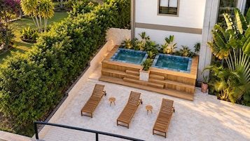 Zona de piscina en la azotea con sillones de madera y una pequeña mesa, rodeada de exuberante vegetación y un muro de piedra.