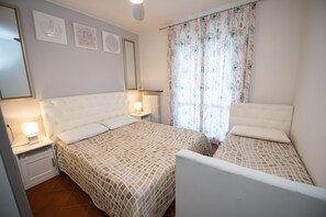 A bedroom with two beds, a nightstand, a bedside table, and a window with floral curtains.