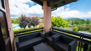 Ein Balkon mit Korbmöbeln und Blick auf ein Schwimmbad und Grünflächen.
