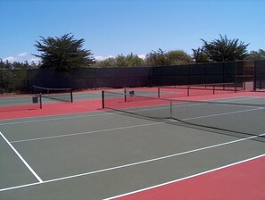 Ein Tennisplatz mit mehreren Spielfeldern, umgeben von einem Zaun und Bäumen.