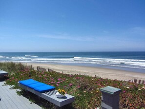 Blick auf einen Strand mit einer Holzterrasse, einem blauen Liegestuhl und einer Blumenvase.