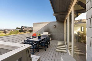 An outdoor deck with a dining table and chairs, a grill, and a view of the beach.