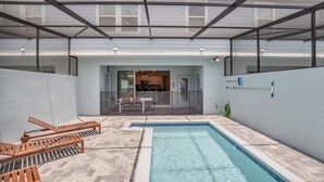 Una piscina con sillas de descanso, un porche cubierto y vista hacia la casa.