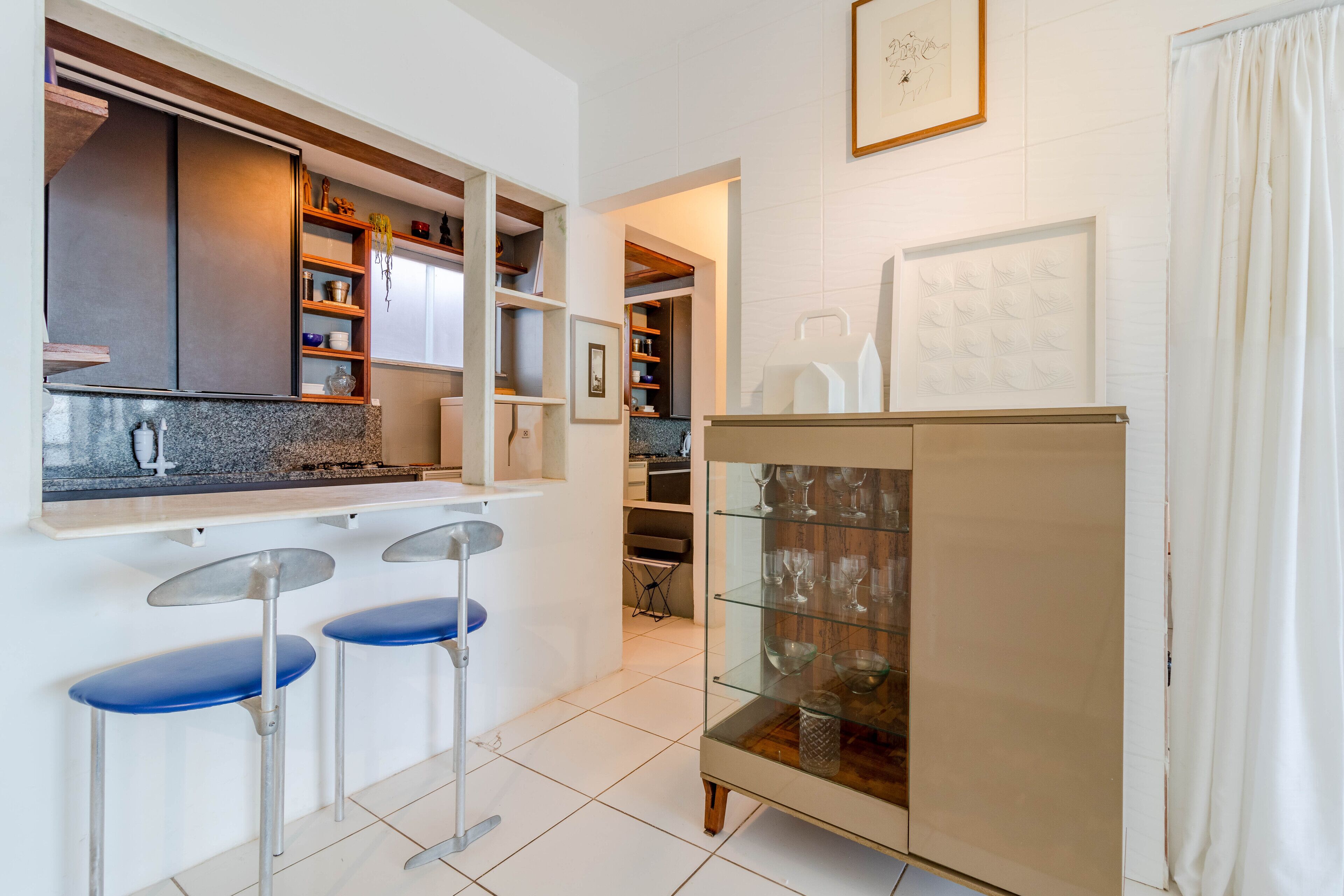 A modern kitchen with a built-in bar area, a glass cabinet with wine glasses, and a dining area with bar stools.