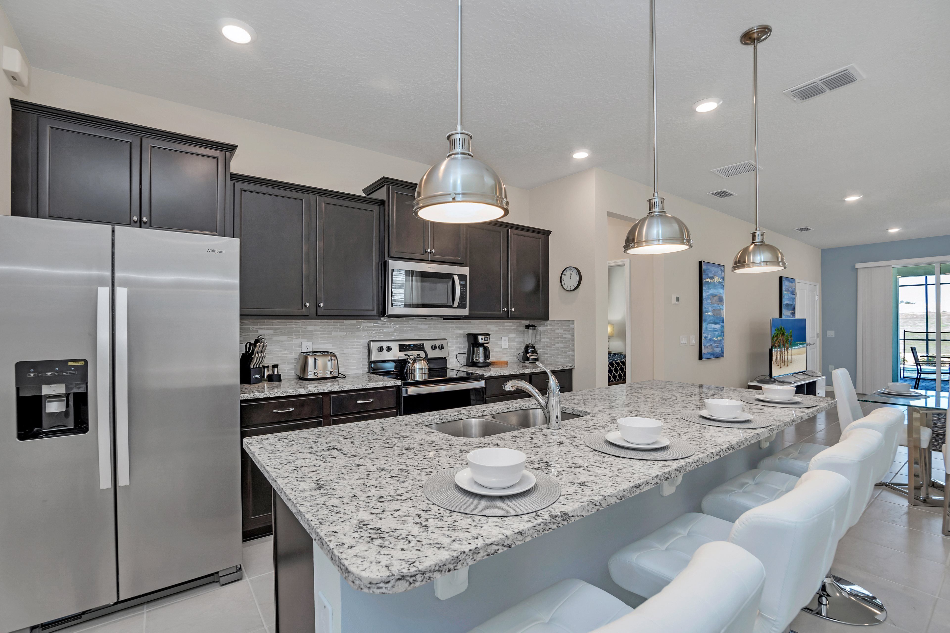 A modern kitchen with dark cabinets, stainless steel appliances, a granite countertop, and a bar area with white bar stools.